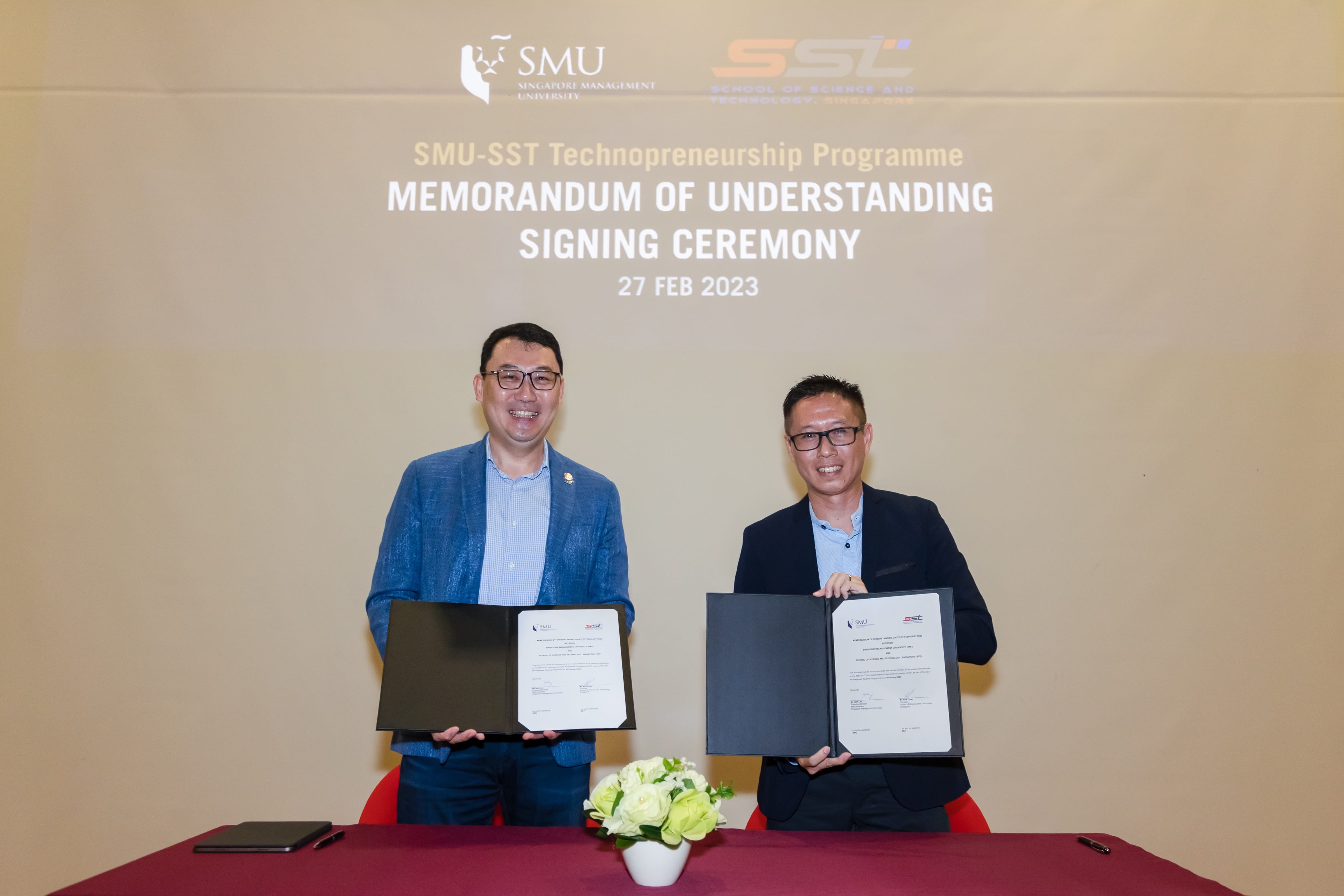 Two men hold signed MOU documents at the SMU-SST Technopreneurship Programme signing ceremony on 27 Feb 2023.